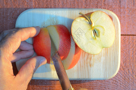 日落时在红褐色背景的木板上用一把刀砍苹图片