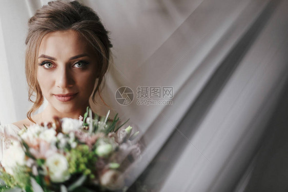 华丽美的新娘与花束在柔和的光线下摆在窗口图片