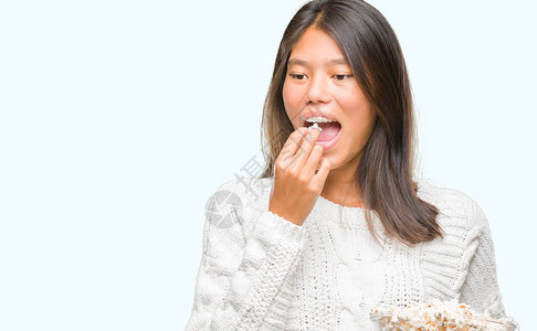 年轻的亚洲女在孤立的背景中吃爆米花自信地表现在聪明的面孔图片