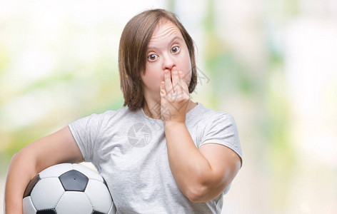 患有唐氏综合症的年轻成年女拿着足球在孤立的背景上用手捂住嘴图片