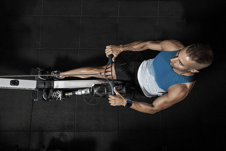 上面的体育运动员腿假肢在健身房打划船机工作他正在图片