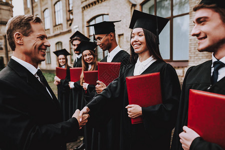 愉快老师握手学生文凭庭院大学完成学业毕业伙计们迎接一群年轻人好心情玩得开心友谊知背景图片