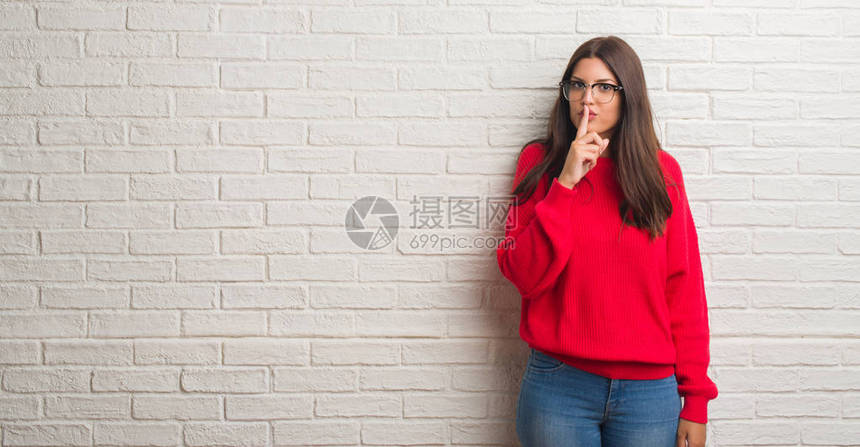 白砖墙上站着的年轻黑发女人要求用手指对嘴唇保持安静图片