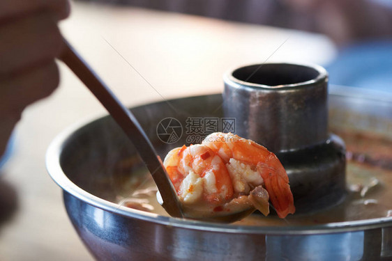 一只手从餐厅的一锅冬阴功中取出美味的虾图片