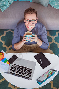 在休息时在家工作喝着咖啡的年轻笑男人图片