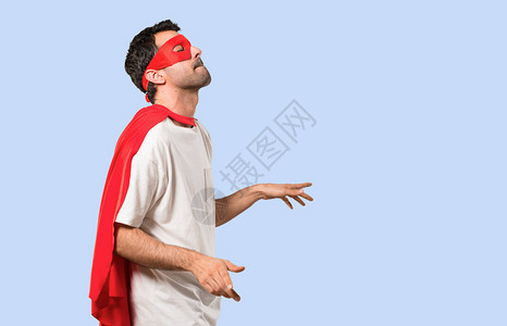 戴着面罩和红色斗篷的超级英雄男子在孤立蓝背景的派对上聆听音乐的同时图片