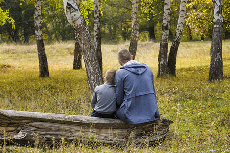 父亲和儿子坐在秋天森林的原图片