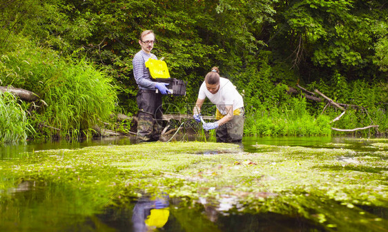 男人和女人科学家环保主义者站在河里女人取水样并将其倒入试管中拿图片