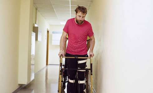 年轻的残疾男子手持步行架穿过康复诊所走廊的画像图片
