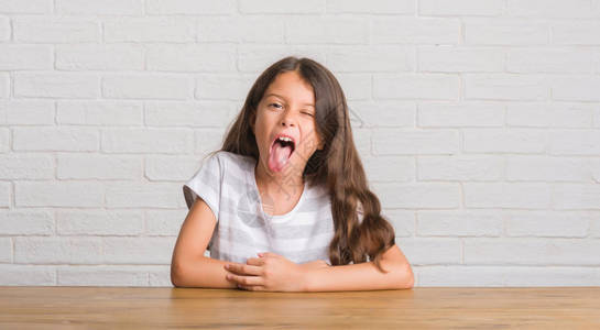 坐在家里桌子上坐着的年幼的西班牙小孩用可笑的表情来表达图片