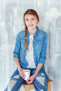 咖啡厅外景穿着牛仔裤牛仔夹克和白色T恤的年轻快乐可爱少女坐在椅子上背景