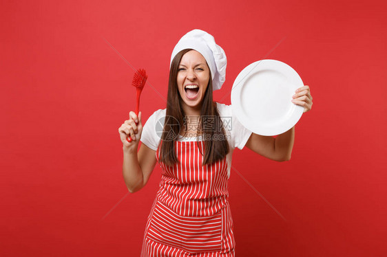 家庭主妇女厨师或面包师穿着条纹围裙白色t恤无边帽厨师帽隔离在红墙背景上女人拿着白盘子用刷子洗碗模拟图片