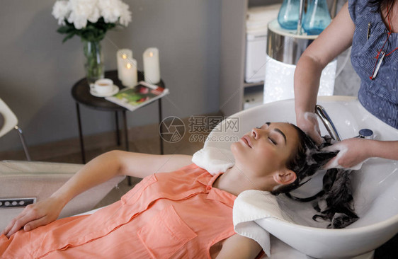 在舒适的美容室里放松和躺在沙发上的宁静女人的顶视图美发师正在用洗发水图片