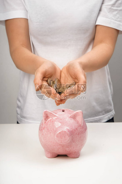 女人把硬币放到桌上的存钱罐里图片