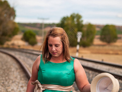 一位身穿绿色派对礼服头戴草帽的金发女子在铁轨上的肖像图片