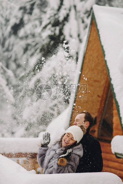 时尚的情侣在冬天雪山的背景下在木屋里玩雪图片
