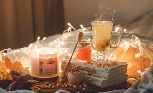 旧书蜂蜜蜡烛和秋叶上的沙棘浆果和生姜茶图片