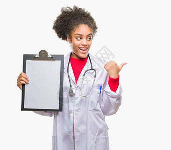 年轻的美国女医生拿着剪贴板在孤立的背景上指向并用拇指举起手面图片