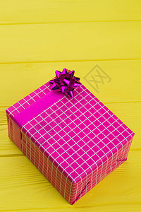 在黄色木制背景上用粉红色纸包裹的礼物盒图片