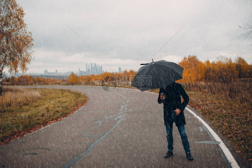 穿黑大衣的年轻人在雨中带着图片