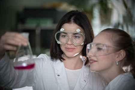 化学实验室两个年轻女人拿着瓶装粉红色液体的酒图片