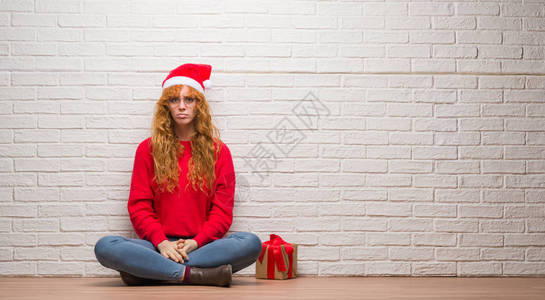 坐在砖墙上戴着圣诞帽子的年轻红发妇女感到沮丧和忧心忡愤怒和恐惧哭泣图片