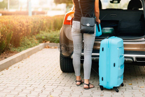 年轻女子将两个蓝色塑料手提箱装上汽车后备图片