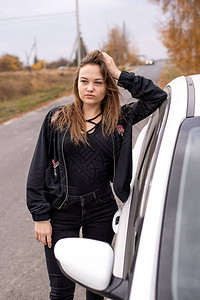 白车旁边秋天的黑衣年轻美女在图片