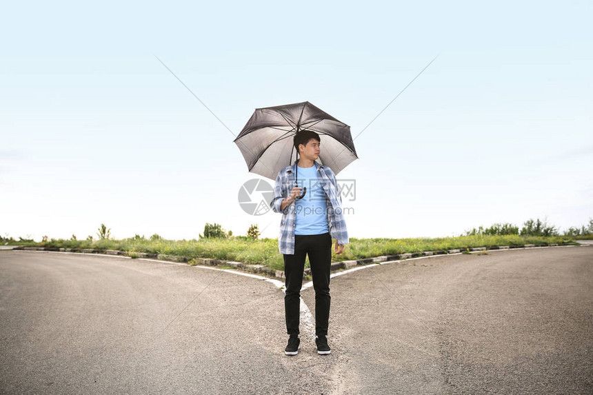 在十字路口站着有伞的青年男子图片