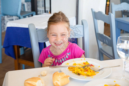 四岁金发女孩的肖像坐在餐厅里大笑吃西图片