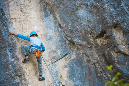 一名儿童登山者在岩石上攀爬戴头盔的男孩爬上悬崖坚强的孩子在自然浮雕上克服了艰难的攀登路线极限运动背景图片