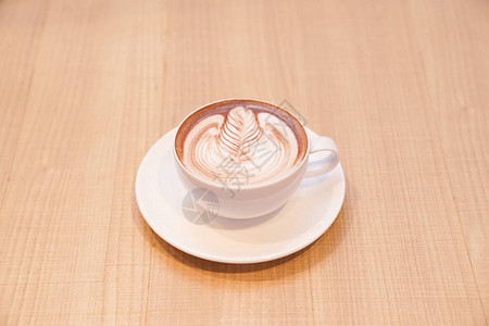 用白咖啡杯装着可爱的拿铁叶热咖啡放在木制桌图片