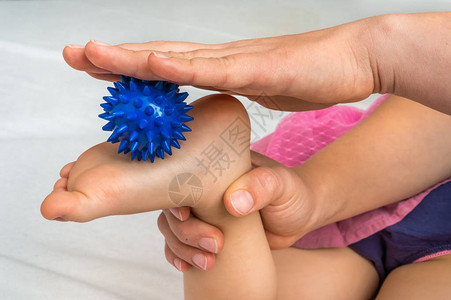 母亲用蓝色按摩球为婴儿做脚按摩给图片