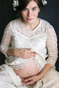 一名身着白丝带礼服头发上插花的怀孕女图片