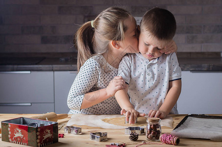 节日甜食概念姐在做圣诞饼干时亲吻哥木桌上的节日饼干的图片