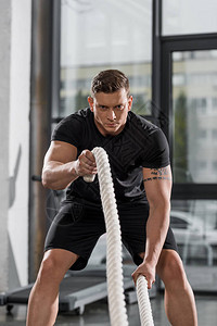 英俊的肌肉健美运动员在健身房用绳索锻炼图片