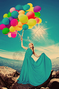 豪华时尚髦的女人手上拿着气球在海滩上对着天空图片