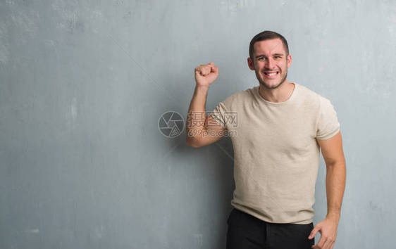 年轻的高加索男子在灰色的垃圾墙上愤怒和疯狂地举起拳头沮丧和愤怒图片