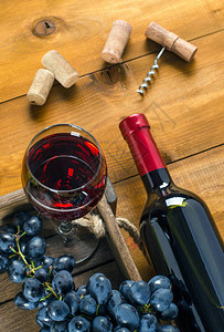 红酒券木制背景上的一瓶和一杯红酒葡萄软木塞和一个开瓶器背景
