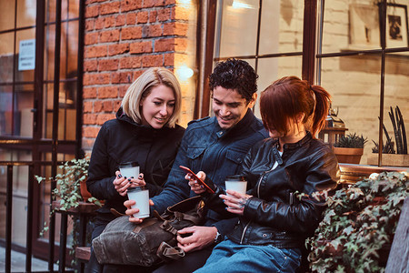 三个快乐的朋友在外边咖啡馆附近坐着时背景图片