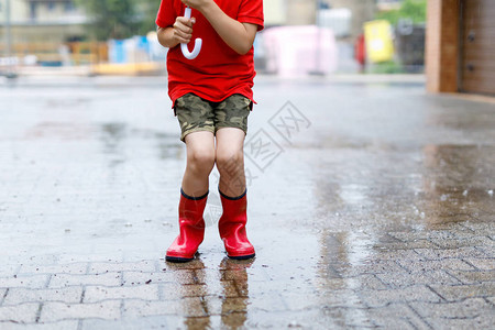 穿着红色雨靴的孩子跳进水坑特写孩子玩得开心泼水的夏雨图片
