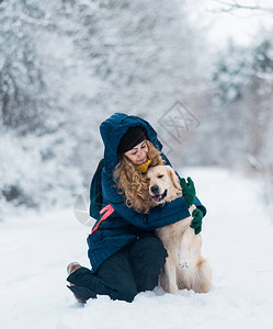 快乐的年轻美女在冬天把雪花从她的手吹到她的狗金色猎犬身上图片