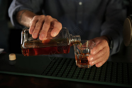 酒男把威士忌倒在酒吧的玻图片