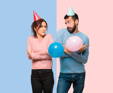 夫妇带着气球和生日帽指向有疑问的支线粉红色和蓝色背图片