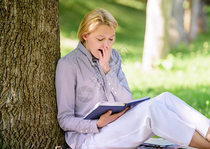 放松休闲爱好概念最好的女自助书籍女孩累了打呵欠坐在公园瘦树干上看书阅读鼓舞人心的书籍畅销书排行榜每个女孩背景图片