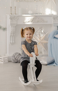 摇滚歌手穿着白色连衣裙的漂亮小女孩像公主一样坐在老式工作室的玩具木马上背景