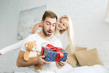 可爱的快乐的小女儿看着惊异的父亲拿着礼图片