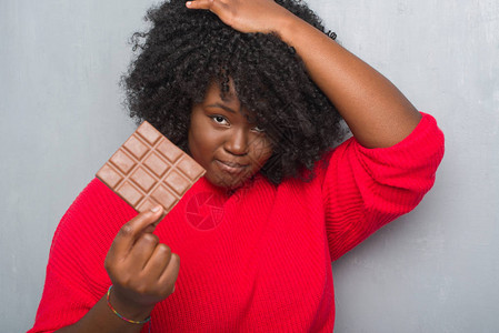 非洲年轻女在灰墙上吃着一根巧克力棒图片