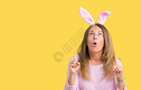 在与世隔绝的背景下戴着复活节兔耳朵的中年黑发女人惊讶地抬起头图片