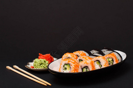 寿司卷和诺瓦米鳄梨片黄瓜在瓷盘上飞的鱼红咸姜和黄图片